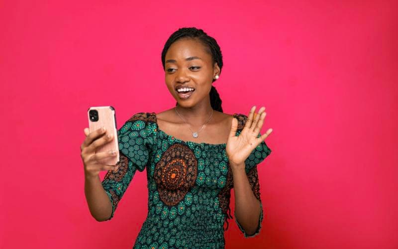 A young woman smiling and waving at her phone