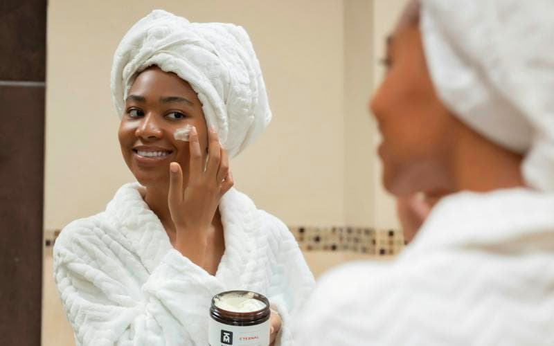 A woman applying face cream in the mirror