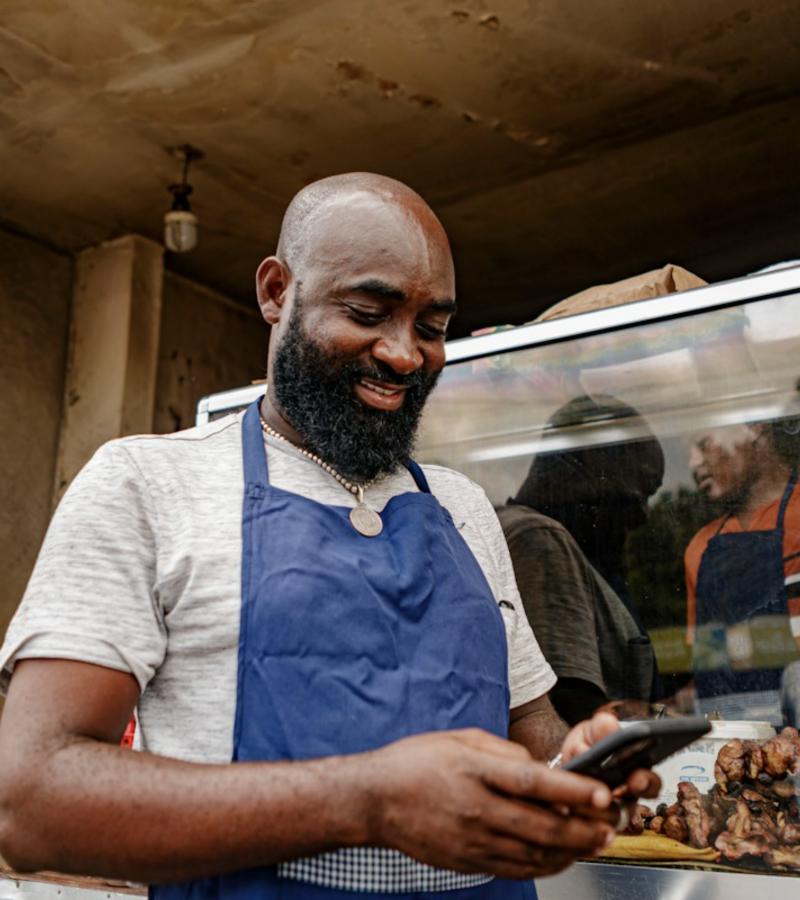 A food business owner smiling at his phone at his stall